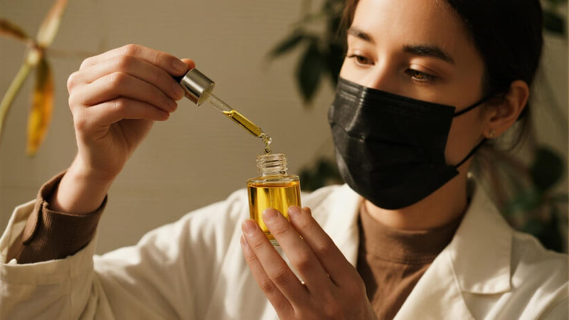 A person using a dropper to add essential oil to a bottle of carrier oil