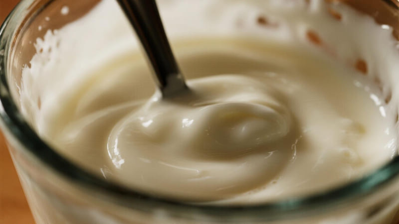 An immersion blender creating a white, creamy emulsion in a beaker